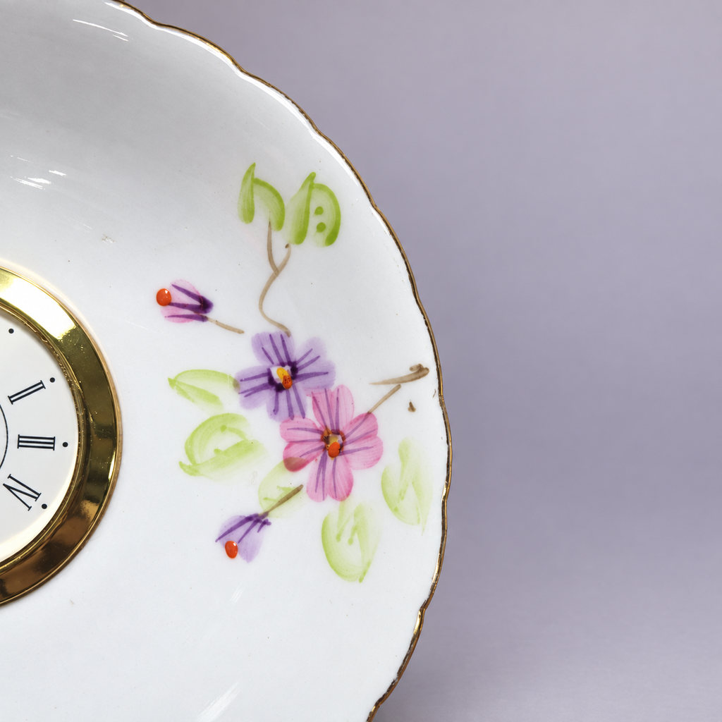 Close-up of the lavender floral plate clock with its gold-tone Roman numeral clock face