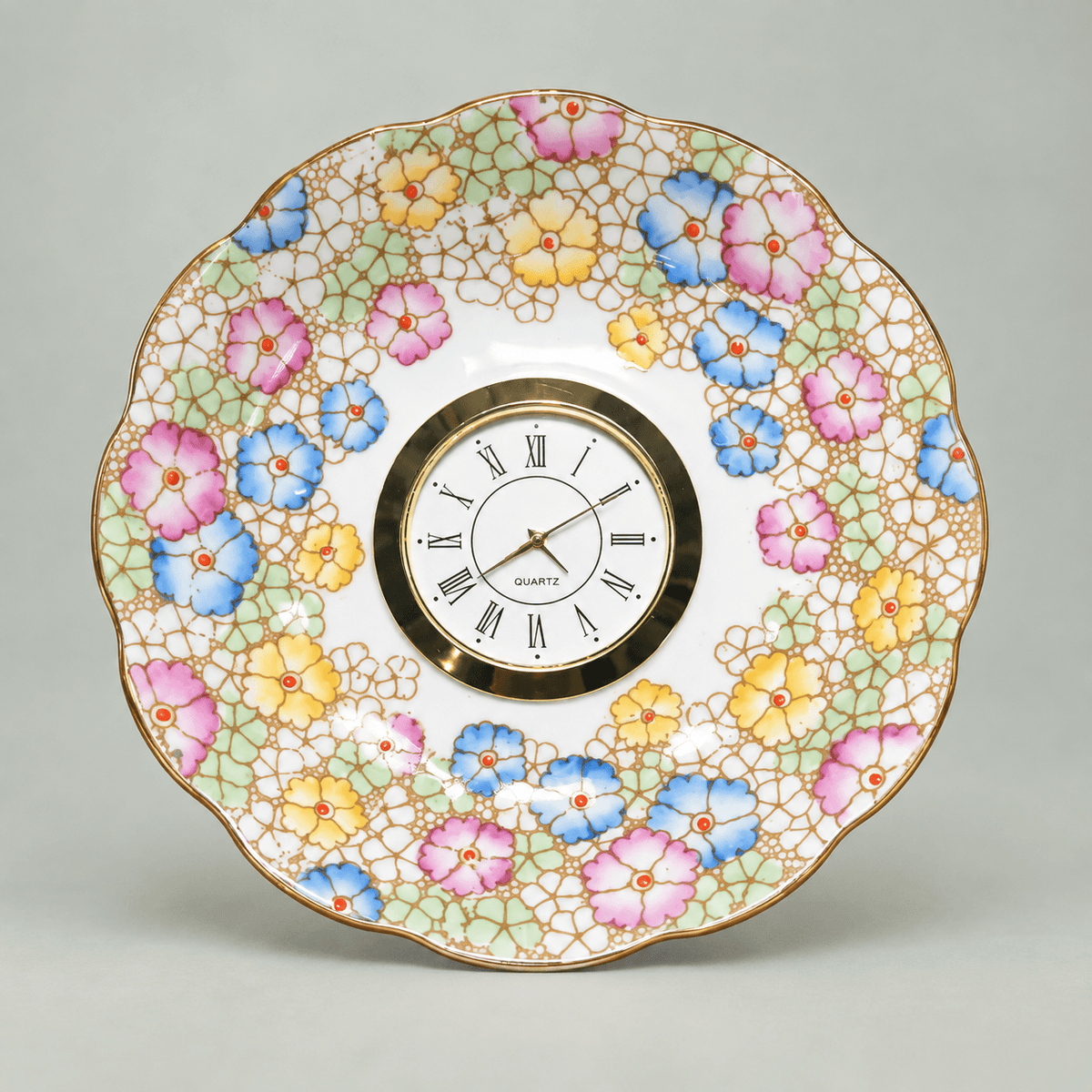 Pastel mosaic china plate clock with pink, blue and yellow flowers, mint-green accents and a gold Roman numeral clock face